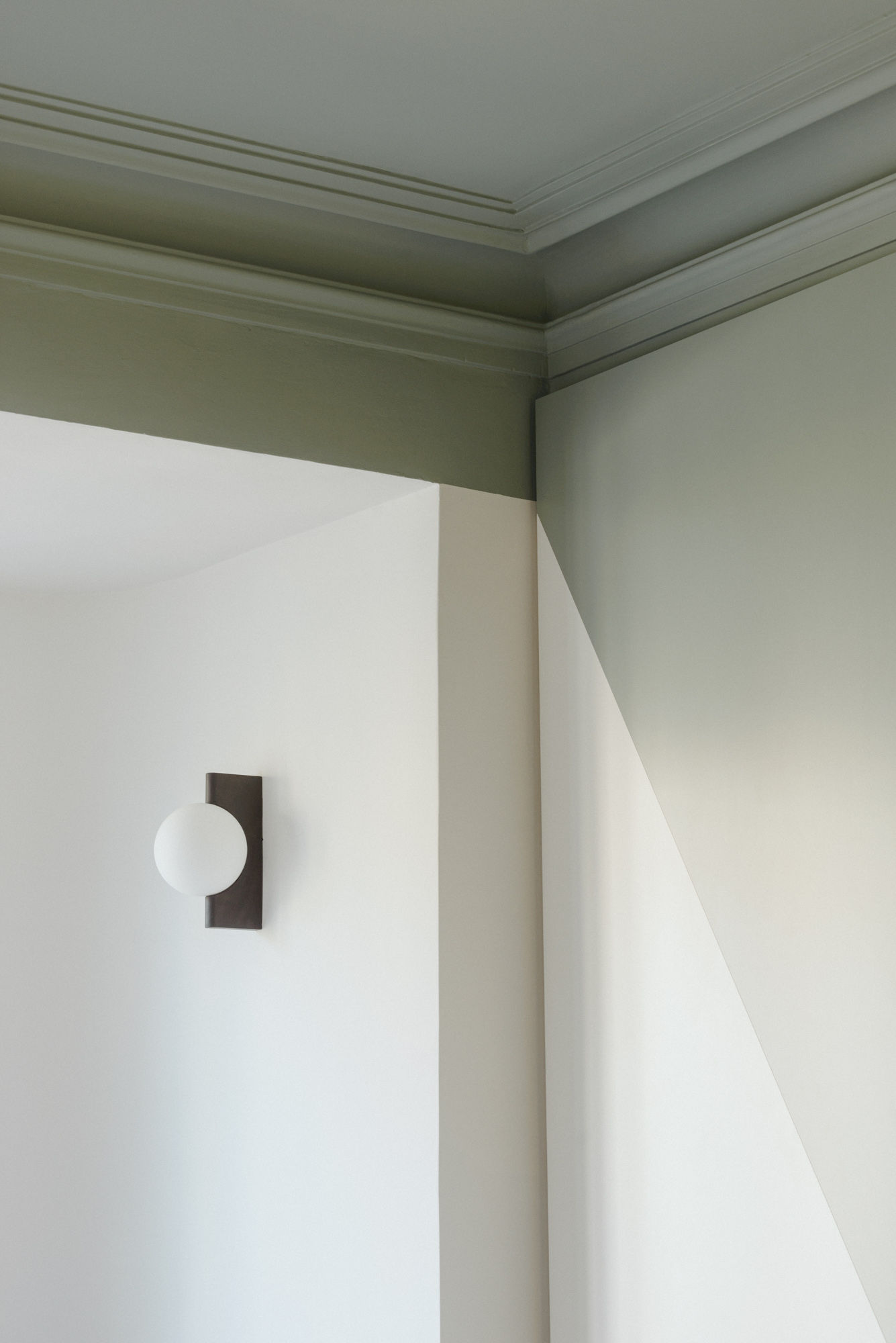 Modern circular spotlight on a white wall with sage green ceiling.