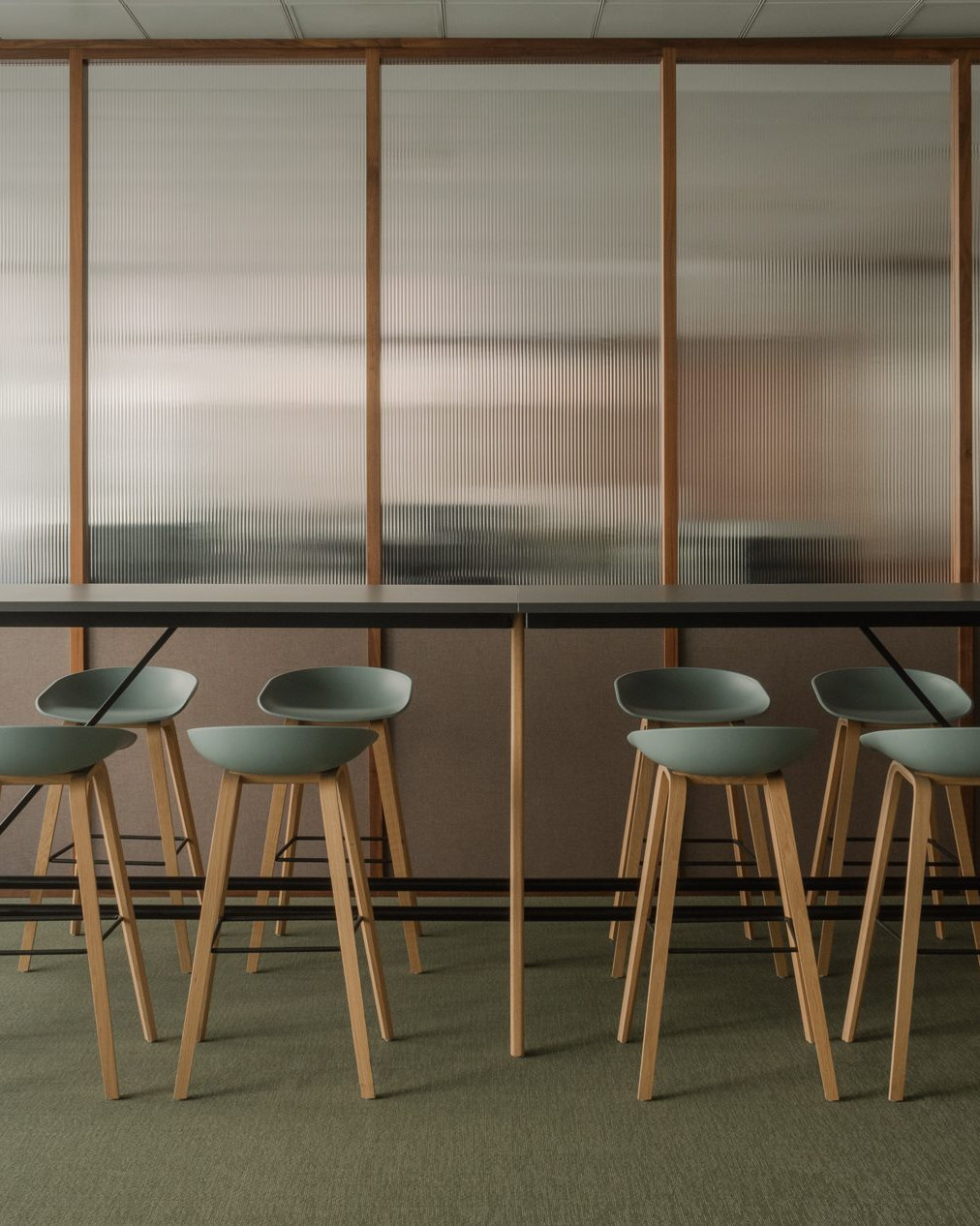 Elegant office break room with green floor, custom dark wood furnishings and walls made of Canaletto walnut panels with fluted glass.