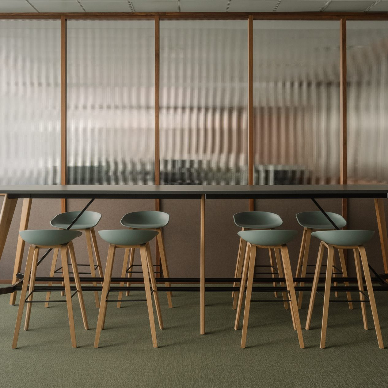 Elegant office break room with green floor, custom dark wood furnishings and walls made of Canaletto walnut panels with fluted glass.