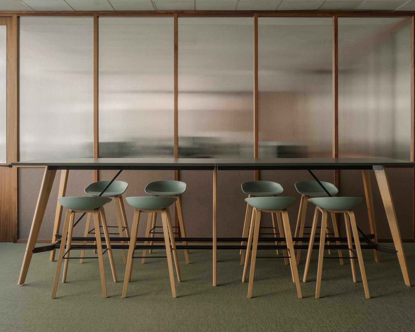 Elegant office break room with green floor, custom dark wood furnishings and walls made of Canaletto walnut panels with fluted glass.
