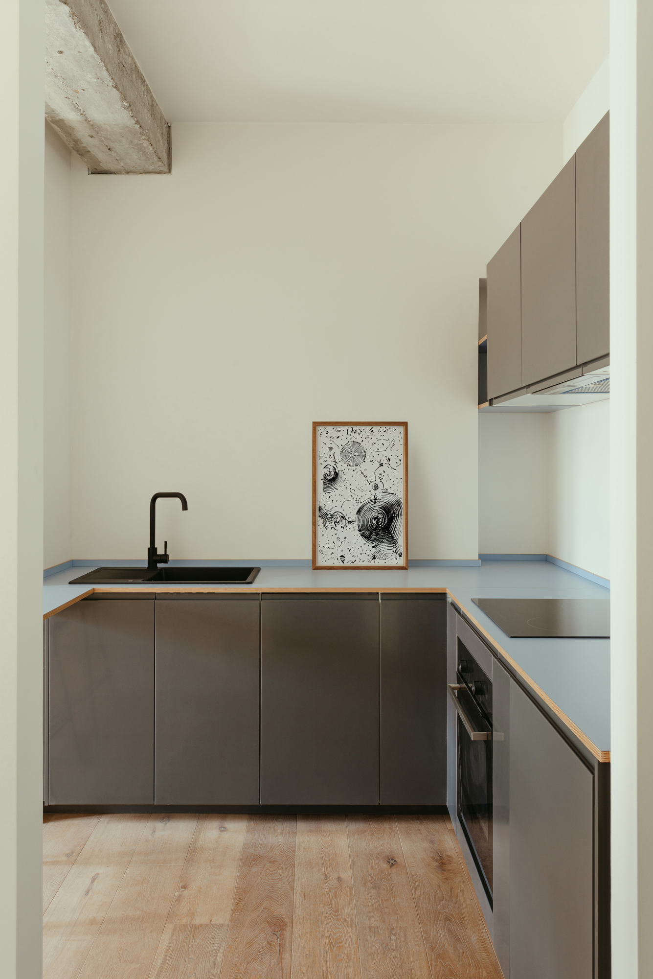 Minimalist kitchen with black cabinets and sink, light blue hob and white walls.