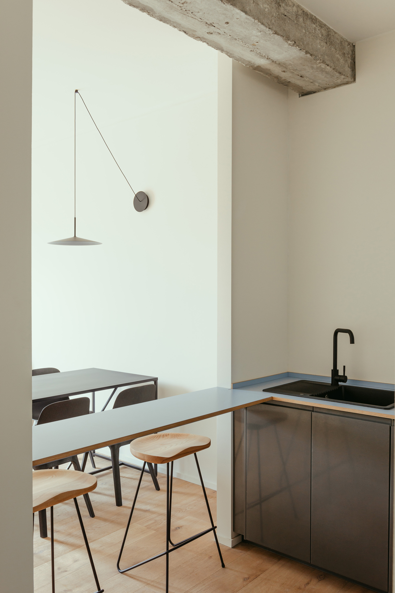 Detail of a custom-designed kitchen with black cabinets and sink, light blue top, light wooden stools and black pendant lamp.